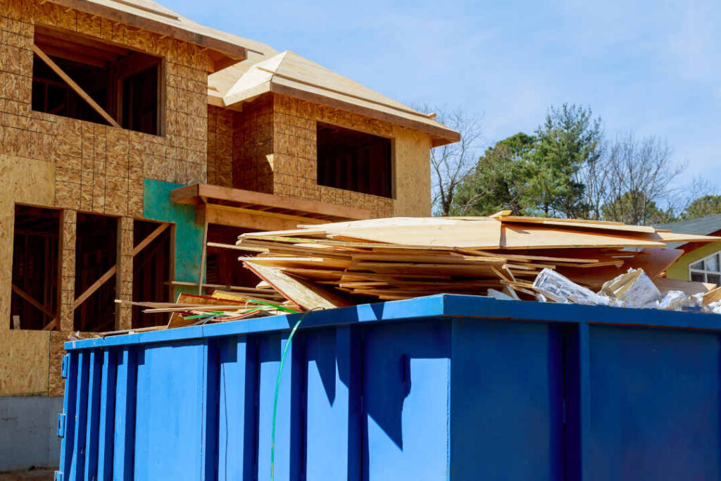 As part of the construction site waste removal process a metal container is used for recycling garbage and a trash dumpster is used for waste disposal