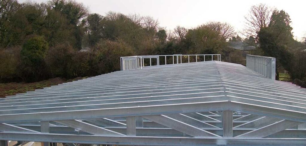 Metal roof under construction, with a galvanised steel frame. The structure is modern, set outside with trees in the background.